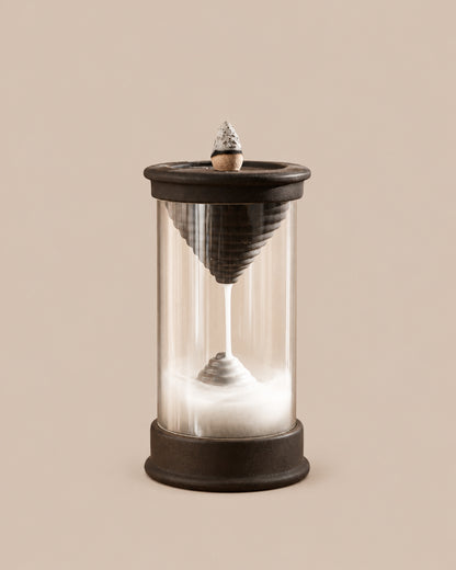 Handmade dark brown Hourglass backflow incense burner with a clear chamber showing a downward stream of smoke, on a beige background.