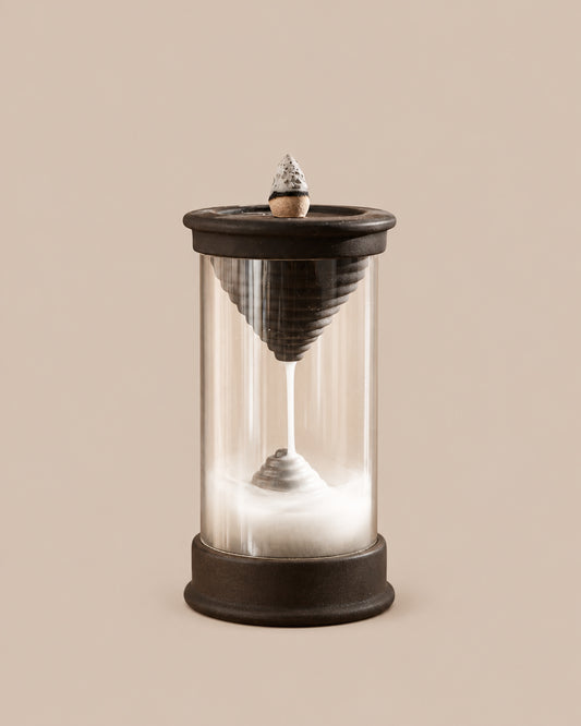 Handmade dark brown Hourglass backflow incense burner with a clear chamber showing a downward stream of smoke, on a beige background.