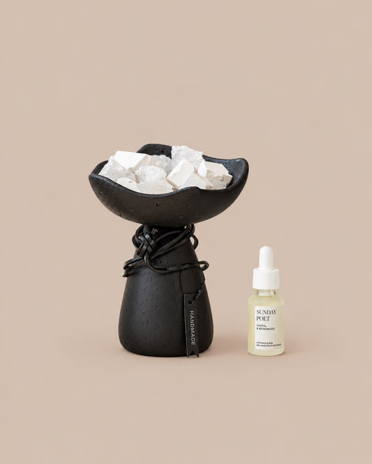 Handmade black cement diffuser vessel filled with clear quartz and white diffuser stones, beside Sunday Poet fragrance oil (15ml).